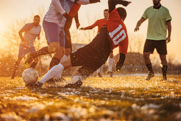 Male soccer match Group of people, male soccer players playing a match on a soccer field on winter day outdoors. Player performing a tackle defending sport stock pictures, royalty-free photos & images
