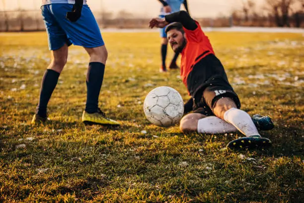 Group of people, male soccer players playing a match on a soccer field on winter day outdoors. Player performing a tackle