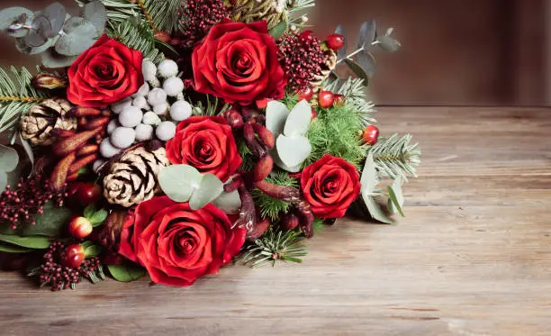 Elegant and romantic bouquet with red roses, eucalyptus leaves, berries, pine branches, pine cones and other beautiful fresh cut flowers lying down on rustic wooden table. Flowers for Christmas, New Year, Valentine`s day, winter wedding celebrations, anniversary gift.