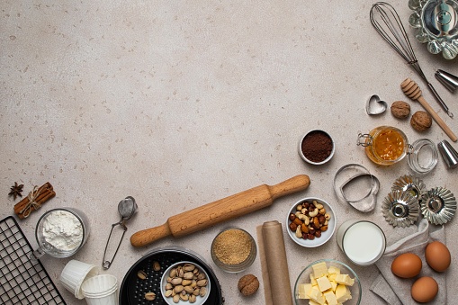Baking background. Baking tools and food ingredients for baking - flour, eggs, sugar, milk, nuts on beige background. Baking or cooking cakes or muffins. Copy space, top view.
