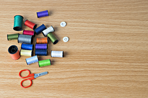 Red scissors,button and colored thread coils on wooden table top view concept needlework and craft.