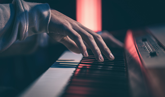 Close-up of male hands playing piano keys in the dark with beautiful lighting.