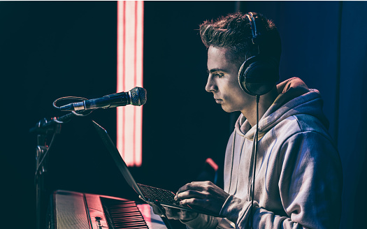 Young man in headphones behind the musical keys with a laptop, sound director, musical creativity.