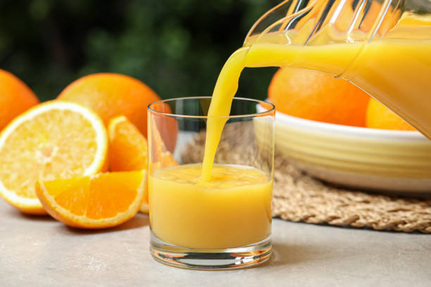 istock Pouring orange juice into glass at light table, closeup 1360157207