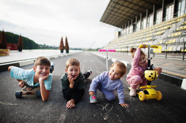 vier kinder im asphalt spielen und haben spaß. sportfamilie verbringt freizeit im freien mit rollern und schlittschuhen. - paint roller paint white painting stock-fotos und bilder