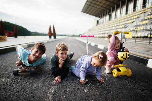 vier kinder im asphalt spielen und haben spaß. sportfamilie verbringt freizeit im freien mit rollern und schlittschuhen. - paint roller paint white painting stock-fotos und bilder