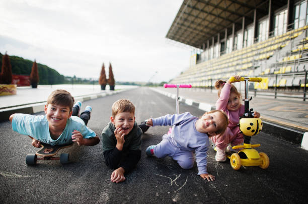 vier kinder im asphalt spielen und haben spaß. sportfamilie verbringt freizeit im freien mit rollern und schlittschuhen. - paint roller paint white painting stock-fotos und bilder