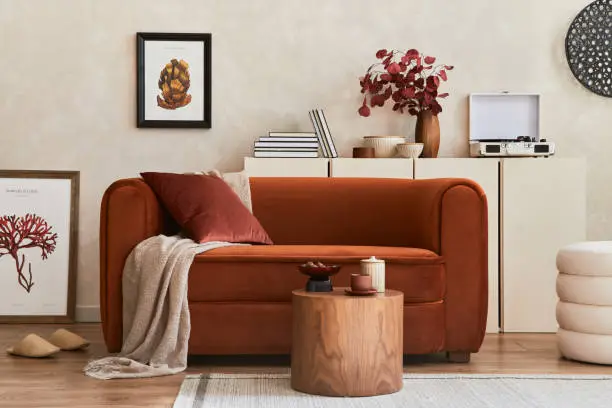 Creative composition of stylish living room interior with mock up poster frame, orange sofa, beige commode, coffee table and stylish personal accessories. Artistic space. Template.