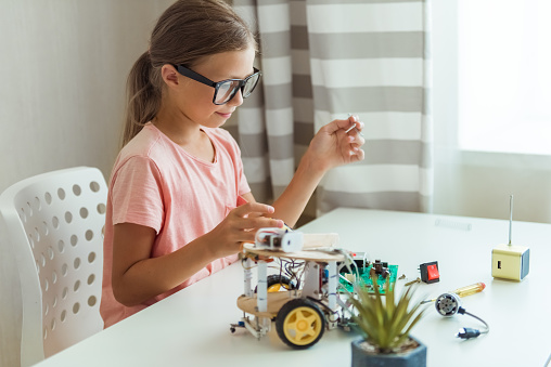 Smiling cute girl constructs metal robot and program it. The boards and microcontrollers are on the table. STEM education, programming. Mathematics. The science. Technologie. DIY