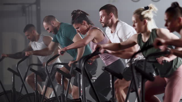 Large group of athletic people having sports training on exercise bikes in a gym. Focus is on woman in the middle.