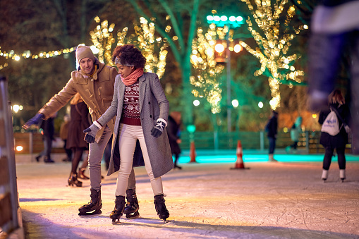 Joyful multiethnic couple enjoying night ice skating together