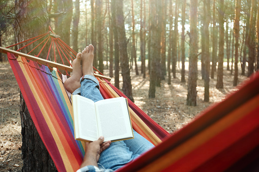 Man with book relaxing in hammock outdoors on summer day, closeup