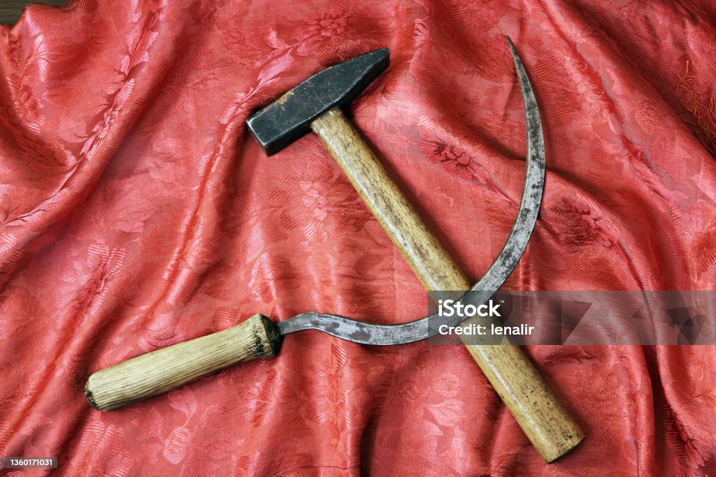 Sickle and hammer on beautiful red shawl Sickle and hammer on rich red shawl as blood Color Image Stock Photo