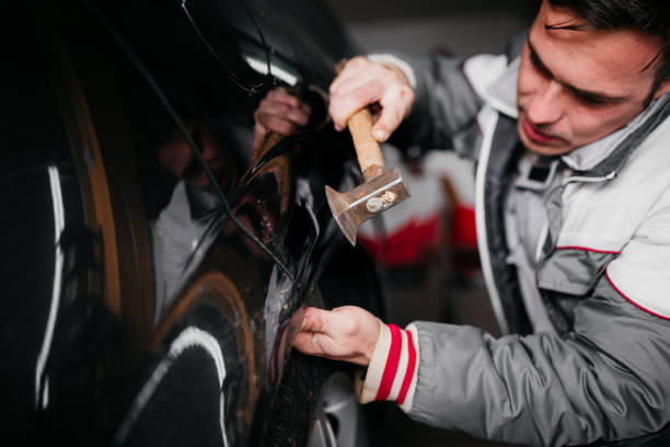 hombre arreglando la abolladura del coche por sí mismo - abollado coche fotografías e imágenes de stock