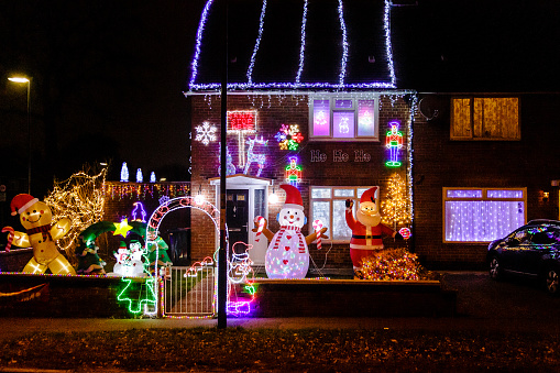 Crawley, UK - 18 December, 2021: a terraced house decorated with fairy lights and festive inflatables, including snowmen and a santa claus, in the front garden for Christmas on a residential street at night.