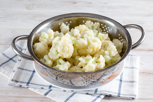 Blanched cauliflower in a colander on a white wooden table