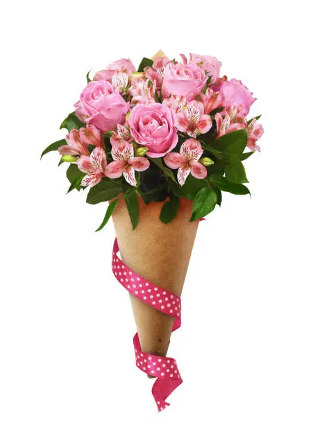 Bouquet of pink roses and alstroemeria flowers in a brown craft paper cornet with silk ribbon isolated on white. Profile view. Holiday present.