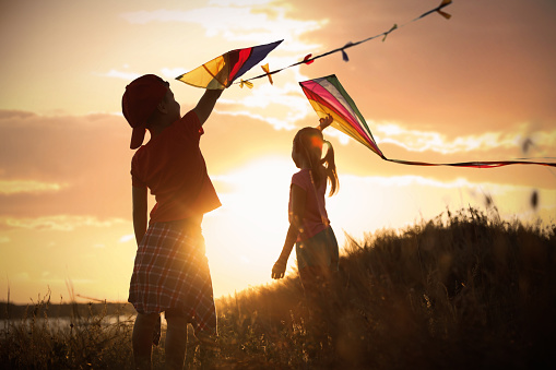 Little children playing with kites outdoors at sunset. Spending time in nature