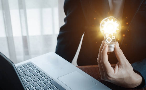 istock The hand of a man with a light bulb And there is a gear icon in it And he is using a notebook computer. 1360183802
