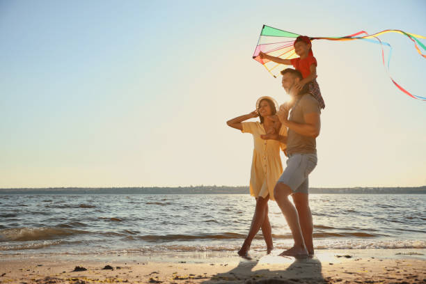 szczęśliwi rodzice i ich dziecko bawiące się latawcem na plaży w pobliżu morza. spędzanie czasu na łonie natury - play time zdjęcia i obrazy z banku zdjęć