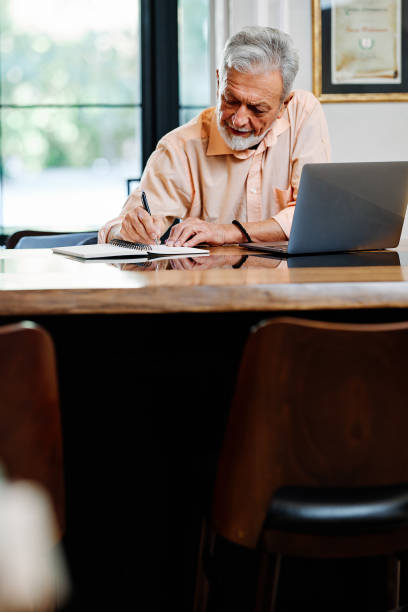 istock A smart senior student is sitting in a cafe and writing down homework. There is a laptop on the table. 1360185400