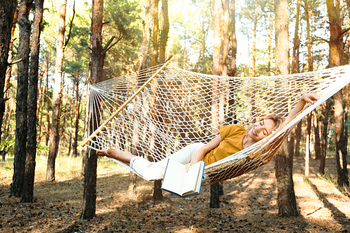 Cute little blond caucasian boy having fun with multicolored hammock in backyard or outdoor playground. Summer active leisure for kids. Child on hammock. Activities and fun for children outdoors