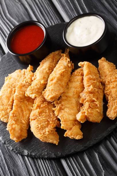 istock Deep-fried chicken strips with spicy sauce and mayonnaise close-up on a black tray. Vertical 1360189823