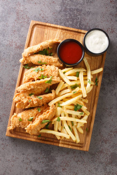 tiras de frango crocante caseiras e batatas fritas de perto na bandeja de madeira. vista vertical superior - chicken tender - fotografias e filmes do acervo