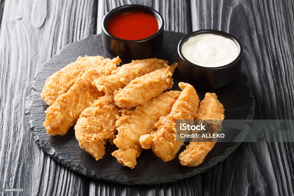 Chicken strips with tomato sauce and mayonnaise closeup. Fast food on black background. Horizontal Chicken strips with tomato sauce and mayonnaise closeup on the plate. Fast food on black background. Horizontal Chicken Meat Stock Photo