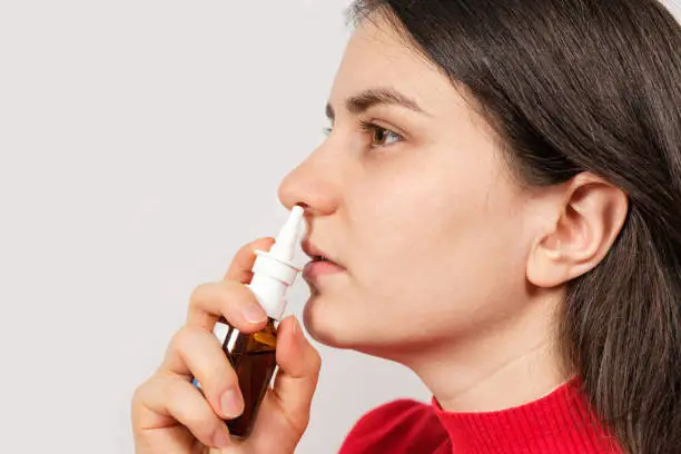 A female patient shoves a spray into the nose to treat rhinitis, an allergy with difficulty breathing. Copy text space
