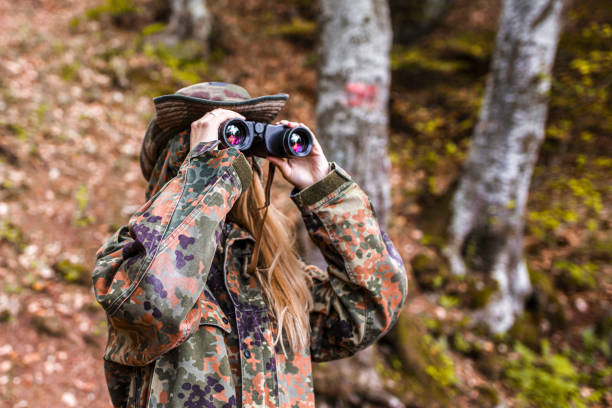 mulher bonita em roupas camufladas olhando através de binóculos na floresta - animais caçando - fotografias e filmes do acervo