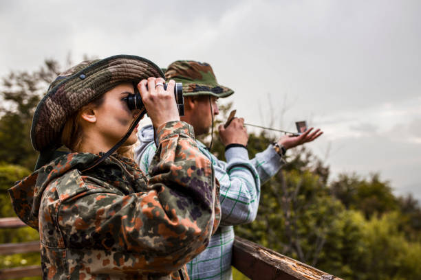 Woman in camouflage clothing looking through binoculars and men looking at a navigational compass Woman in camouflage clothing looking through binoculars and men looking at a navigational compass woodland camo stock pictures, royalty-free photos & images
