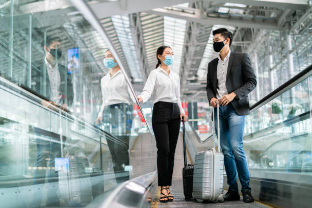 Business New normal concept.Businessman and woman wear face mask on escalator at terminal airport, New normal of people to awareness and protection for prevent coronavirus or covid-19 pandemic. Business New normal concept.Businessman and woman wear face mask on escalator at terminal airport, New normal of people to awareness and protection for prevent coronavirus or covid-19 pandemic. irish travellers photos stock pictures, royalty-free photos & images