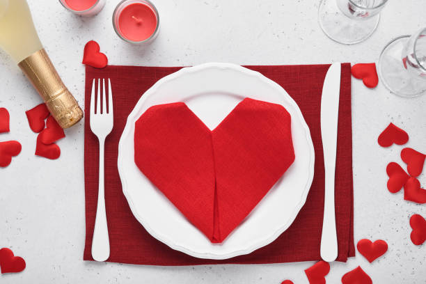 istock Valentinas day table setting white color with white silverware, red napkin folded as heart, candles, champagne, glasses on white background for greetings. Romantic dinner or menu concept. Mock up. 1360198200