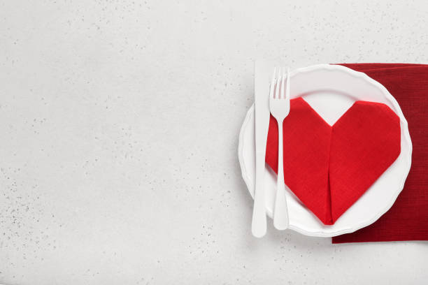 istock Valentinas day table setting white color with white silverware, red napkin folded as heart, candles, champagne, glasses on white background for greetings. Romantic dinner or menu concept. Mock up. 1360198267