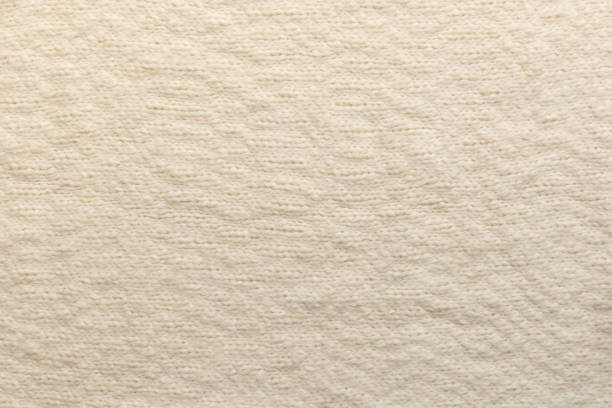Close up texture of handmade knitted woolen fabric in beige, ivory, cream color. Textile background, top view, copy space