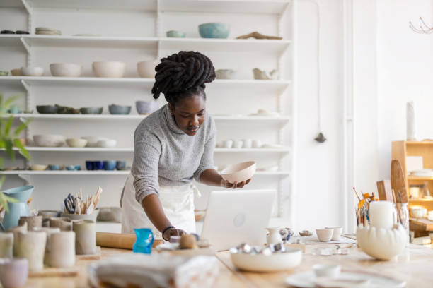 Young female pottery artist using laptop in her workshop