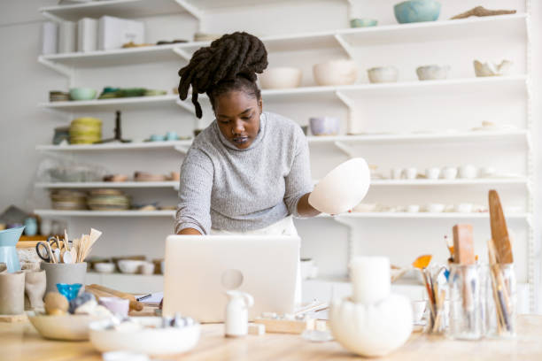 istock Young female pottery artist using laptop in her workshop 1360200401