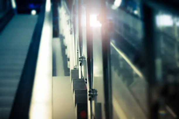 An Escalator inside a public trainstation where the sun is shinig through the exit.