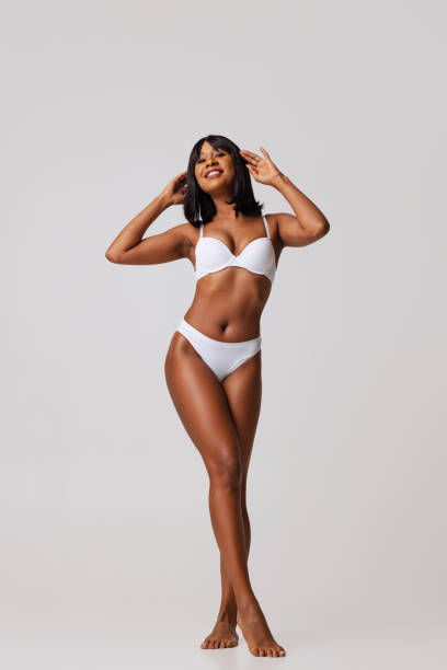 Full-length portrait of young beautiful slim girl in white underwear posing isolated over gray studio background. Natural beauty concept. Tenderness. Full-length portrait of young beautiful slim girl in underwear isolated over gray background. Wellness, wellbeing, fitness, diet concept. Natural beauty of female body. Copy space for ad lingerie stock pictures, royalty-free photos & images
