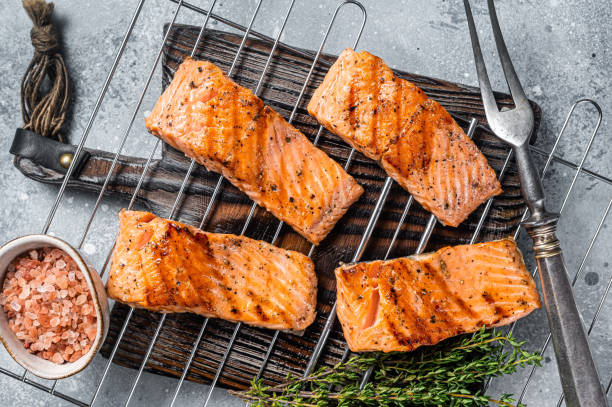Grilled salmon fillets steaks with salt pepper and herb on grill. Gray background. Top view Grilled salmon fillets steaks with salt pepper and herb on grill. Gray background. Top view. grilled salmon stock pictures, royalty-free photos & images
