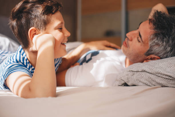 istock Sunny morning. A young boy is lying on the bed, next to his dad, talking. 1360210769