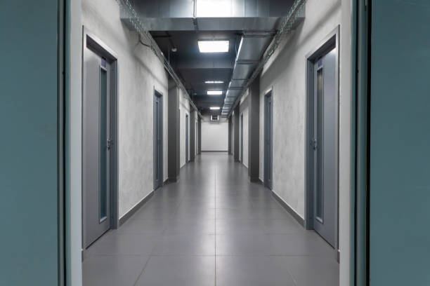 istock Perspective of a long modern empty office corridor with several gray doors. The floor is tiled and the lights are on. 1360211998