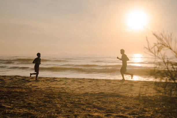 istock silhouette two man run on beach with sunrise and sea background 1360212094