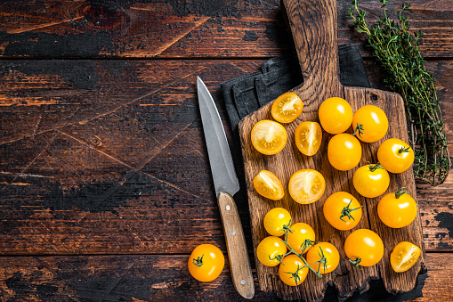 Yellow cherry tomato sliced on a wooden cutting board. Dark wooden background. Top view. Copy space.