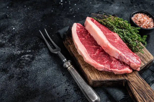 Uncooked Raw rump steak or top sirloin cap beef meat steaks on wooden board. Black background. Top view. Copy space.