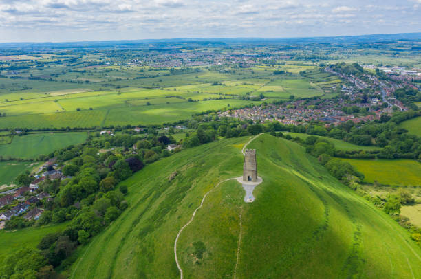 glastonbury tor von drohne an sonnigen tagen gefilmt, ikonisches denkmal mitten in der landschaft - st michaels church stock-fotos und bilder