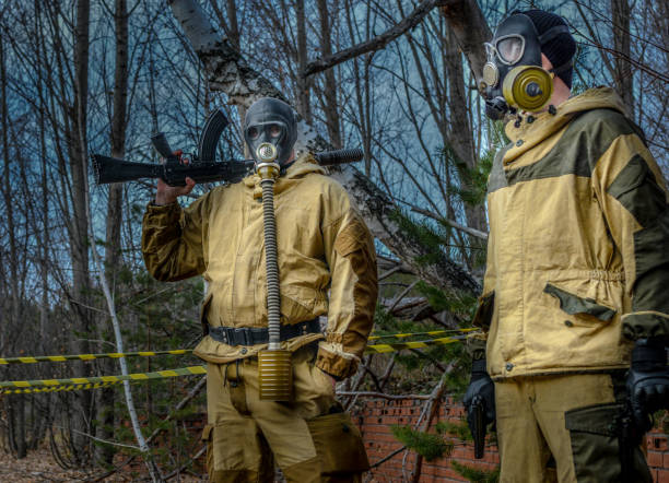 An armed stalker in overalls and a gas mask in a dangerous radioactive zone. An armed stalker in overalls and a gas mask in a dangerous radioactive zone. Apocalypse and nuclear war. Respiratory protection. The stalker walks through the disaster zone. biochemical weapon photos stock pictures, royalty-free photos & images