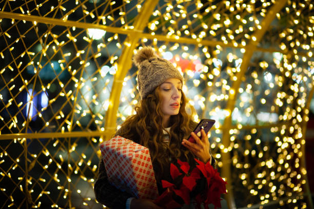 istock Woman Holding Christmas present and using phone 1360217379