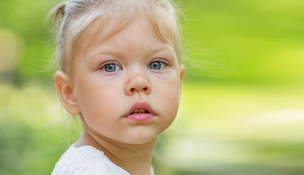 portrait d’une belle petite fille sérieuse de 2 ans regardant l’appareil photo sur fond flou vert avec espace de copie - child caucasian little girls 3 4 years photos et images de collection